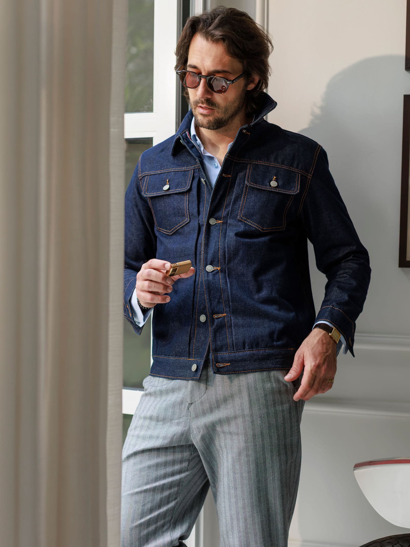 Raw denim trucker over striped trousers by a window